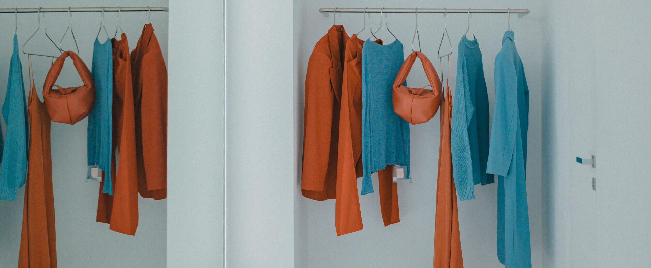 Minimal clothing display with orange and blue dresses, tops, and a small handbag on hangers.