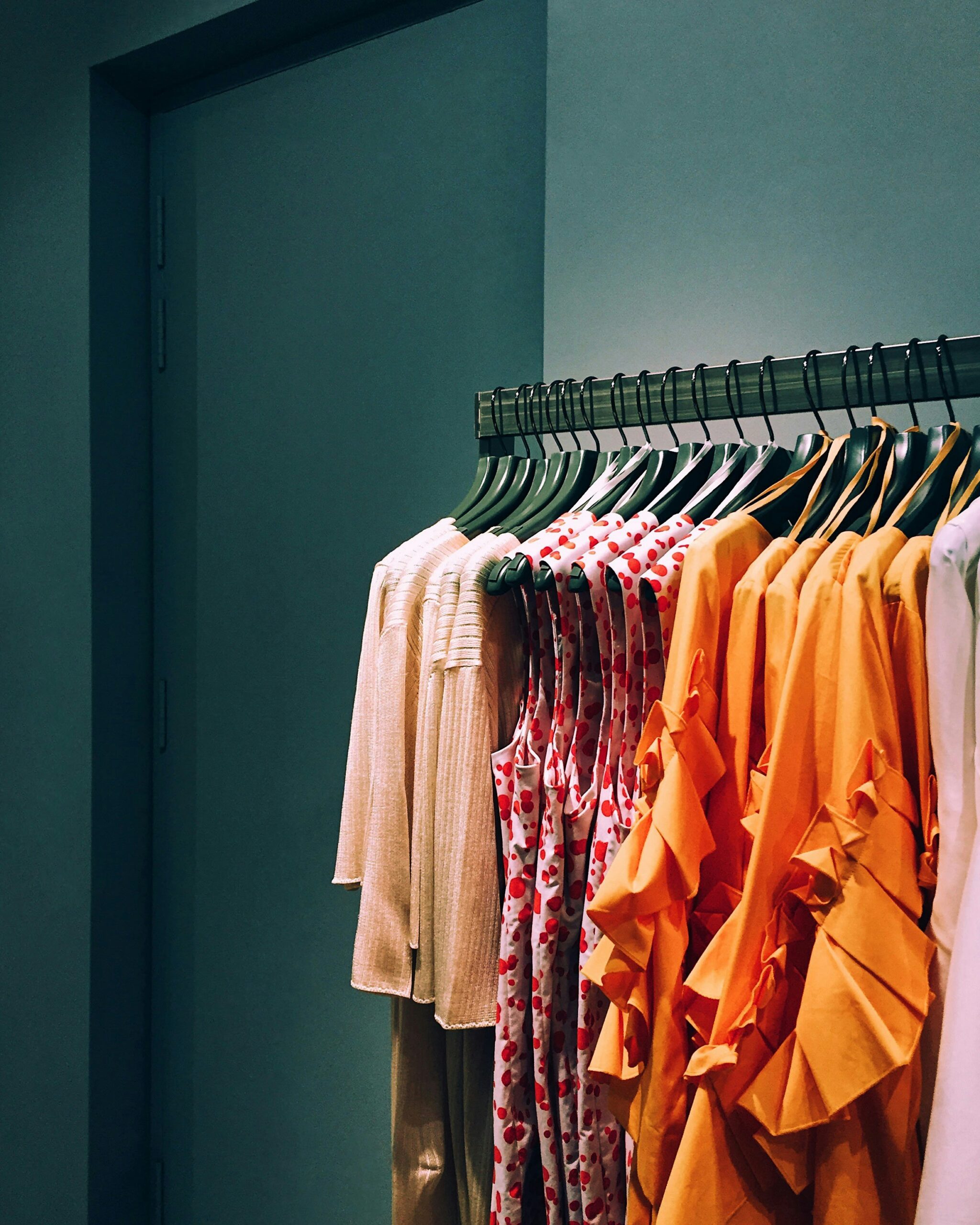 Colorful women’s clothing arranged on a rack, including orange tops and patterned dresses.